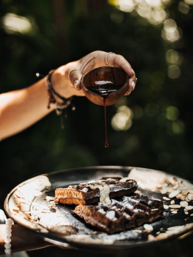 hands-holding-black-plate-with-waffles-peanuts-chocolate-sauce_197531-18183